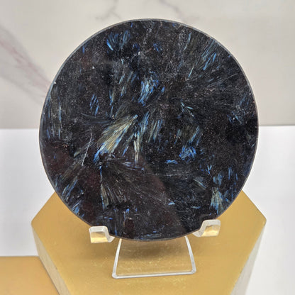 Astrophyllite round carving with varying colors on an acrylic stand on a wood stand against a white background