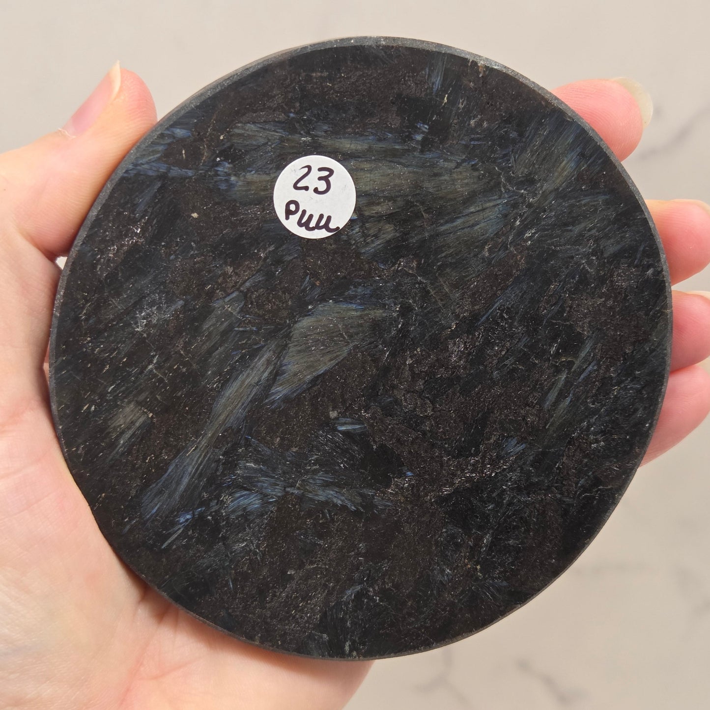 Astrophyllite round carving with varying colors on an acrylic stand on a wood stand against a white background