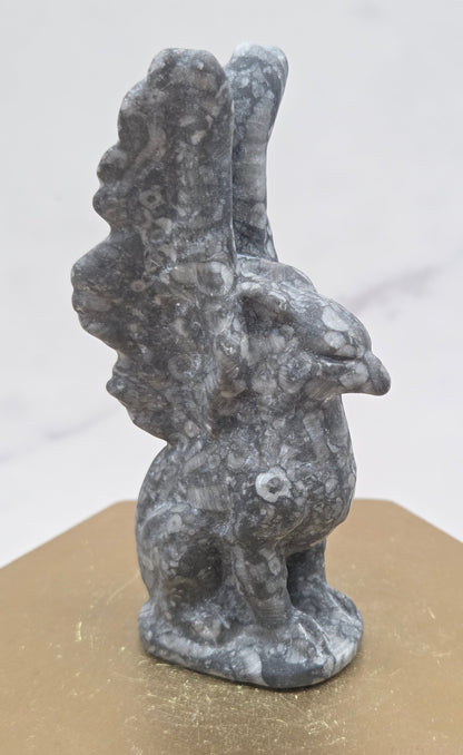 Crinoid Fossil Jasper griffon carving on a wood stand against a white background