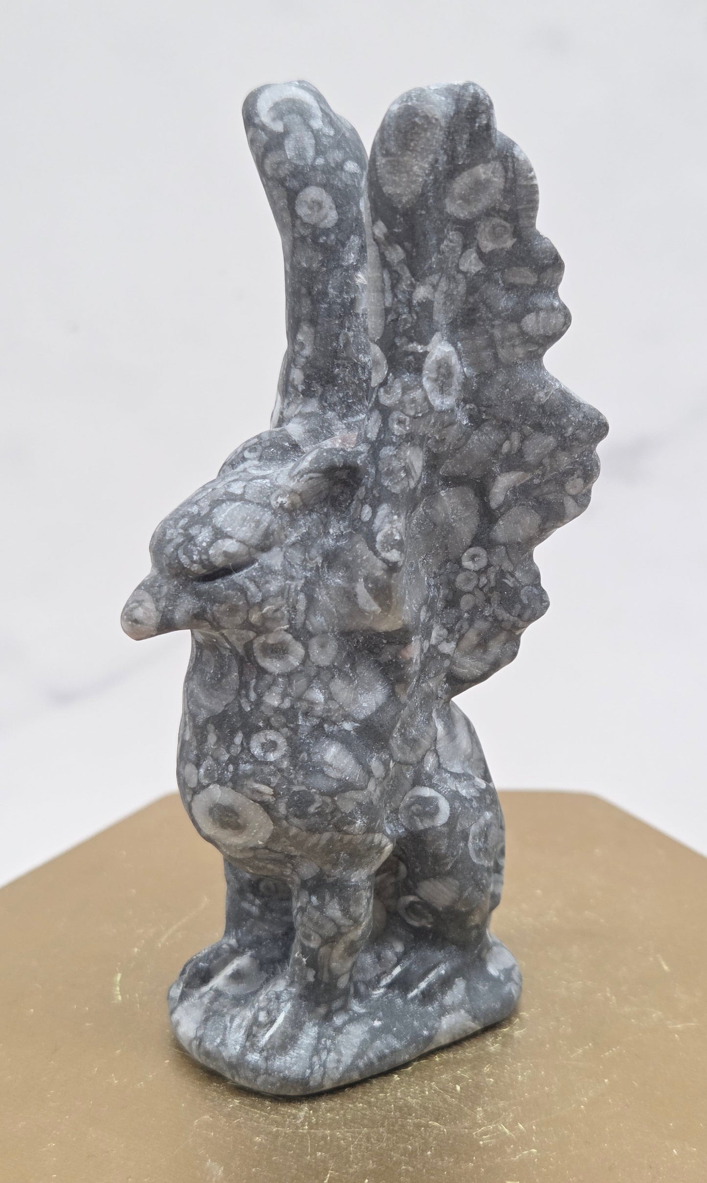Crinoid Fossil Jasper griffon carving on a wood stand against a white background