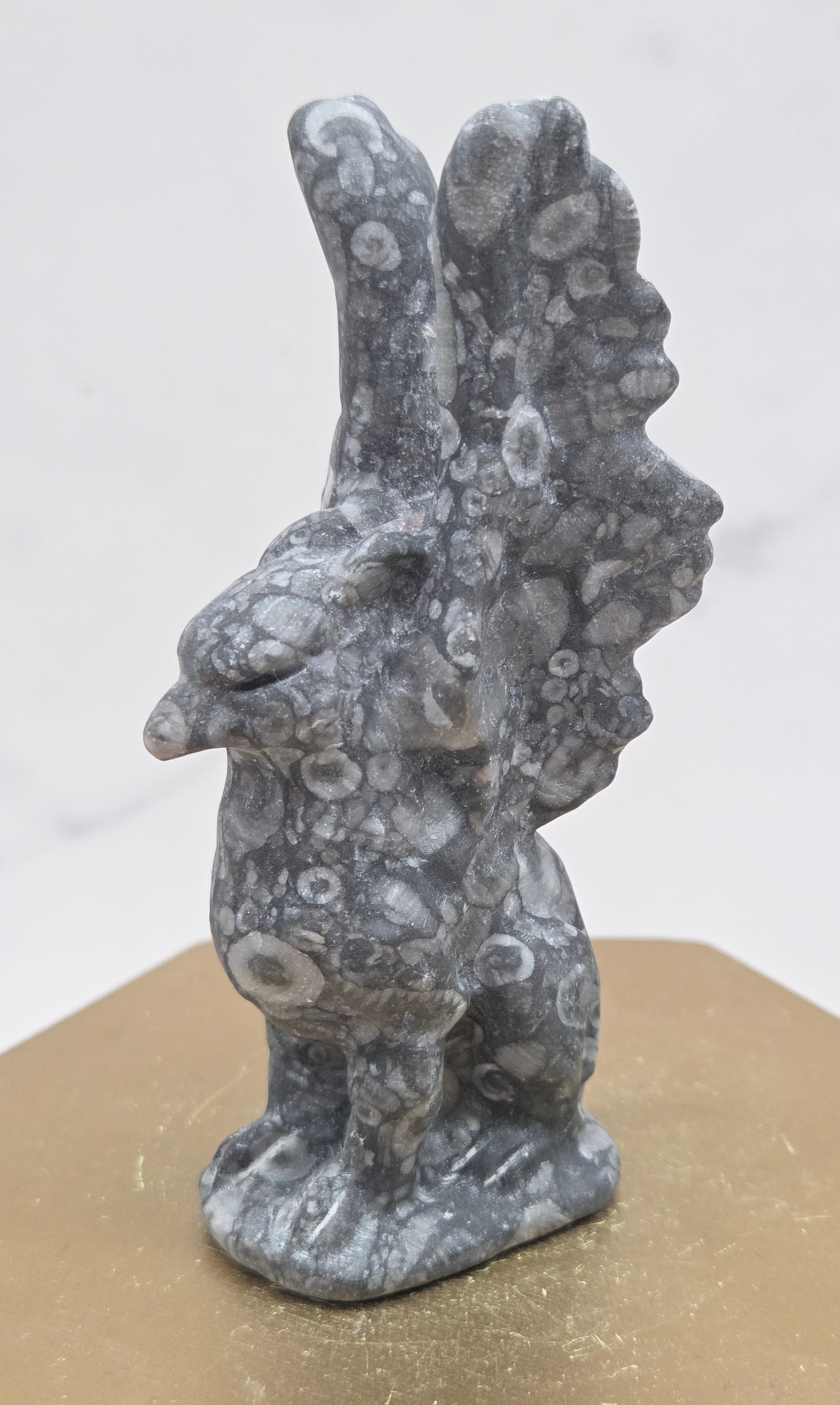 Crinoid Fossil Jasper griffon carving on a wood stand against a white background