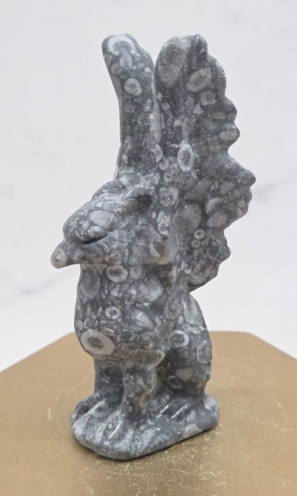 Crinoid Fossil Jasper griffon carving on a wood stand against a white background