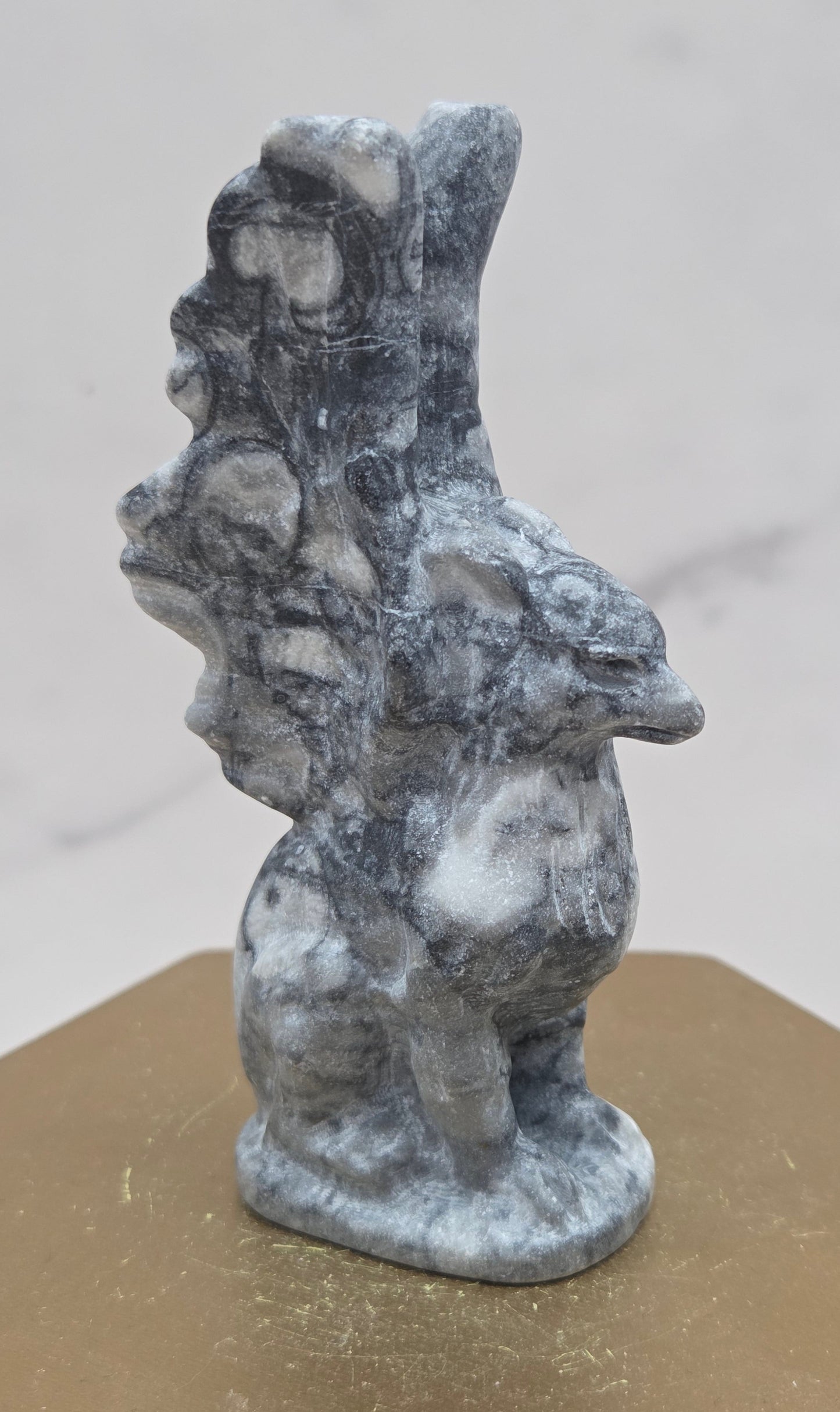 Fossil Jasper griffon carving on a wood stand against a white background
