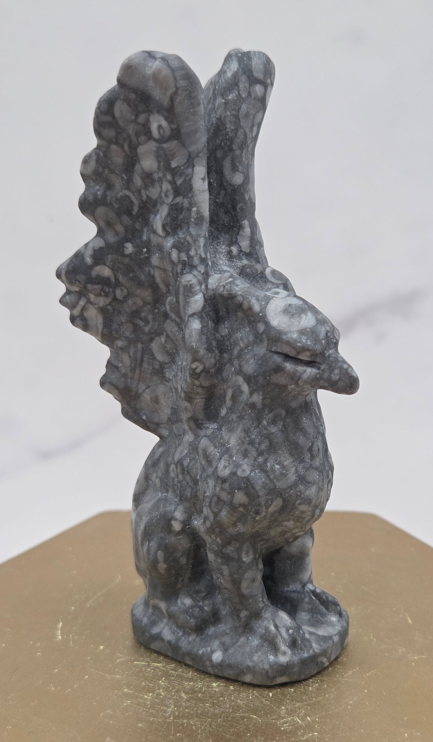 Crinoid Fossil Jasper griffon carving on a wood stand against a white background