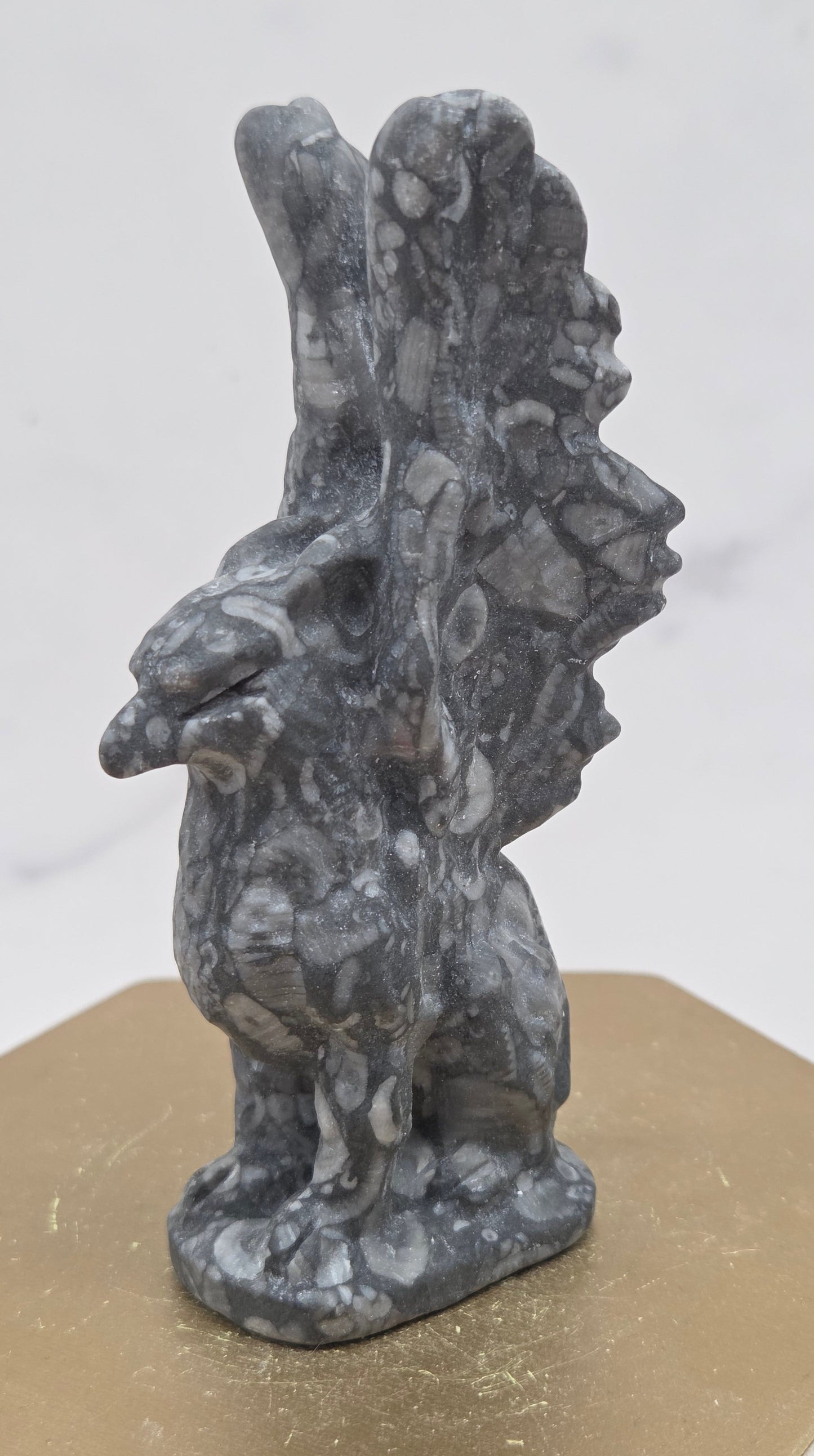 Crinoid Fossil Jasper griffon carving on a wood stand against a white background