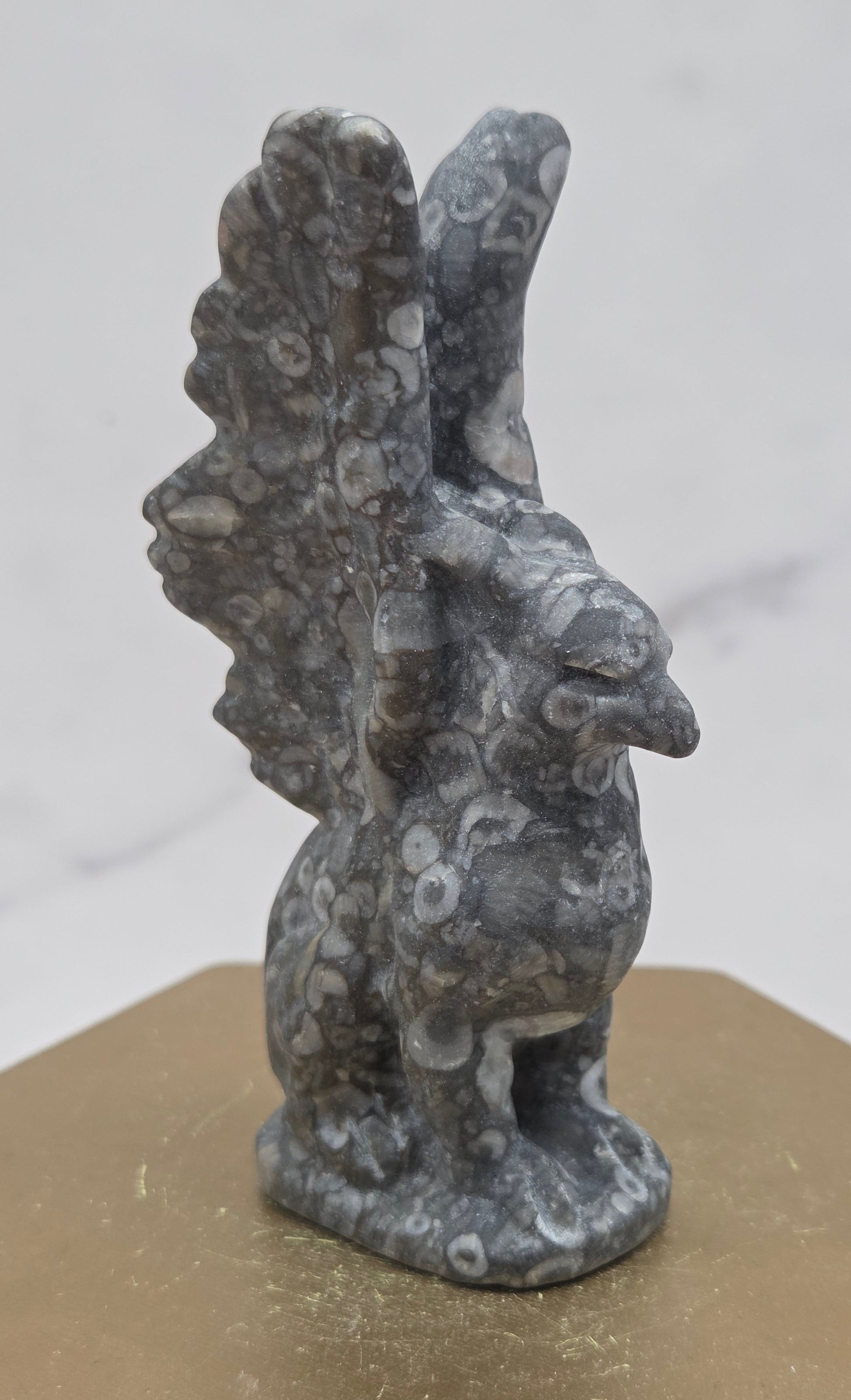 Crinoid Fossil Jasper griffon carving on a wood stand against a white background