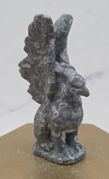 Crinoid Fossil Jasper griffon carving on a wood stand against a white background
