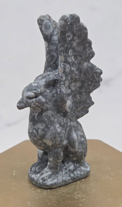 Crinoid Fossil Jasper griffon carving on a wood stand against a white background