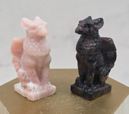 Decorative griffon carvings in pink and black on a wooden surface with a white background