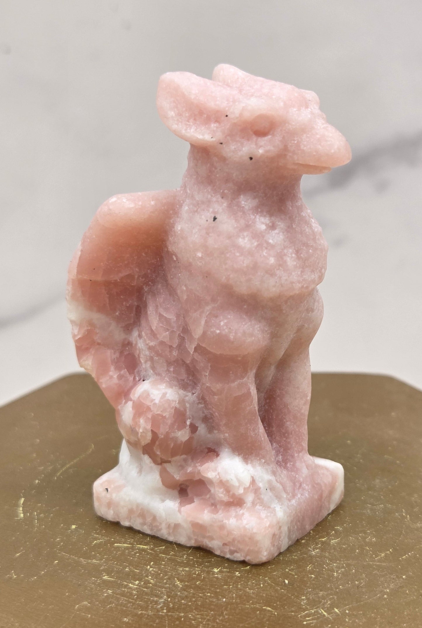 Decorative Pink Opal griffon carving on a wooden surface with a white background