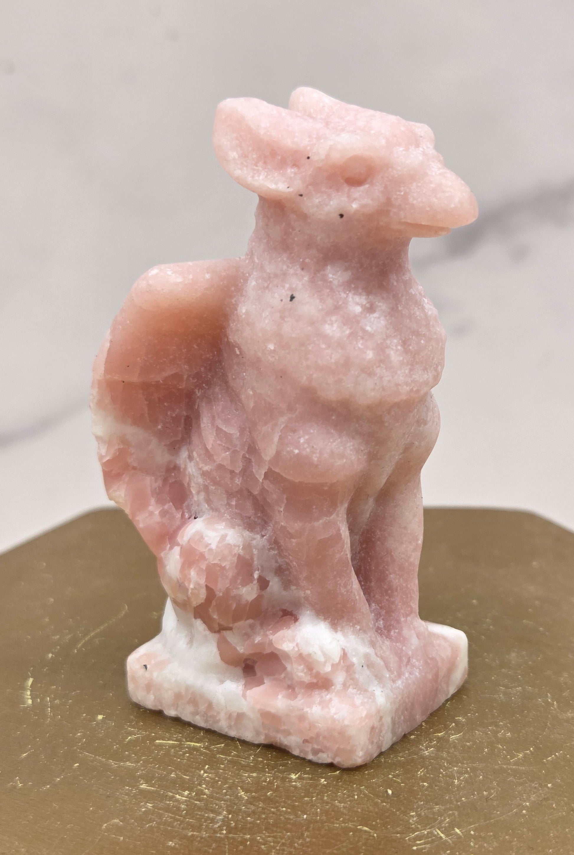 Decorative Pink Opal griffon carving on a wooden surface with a white background