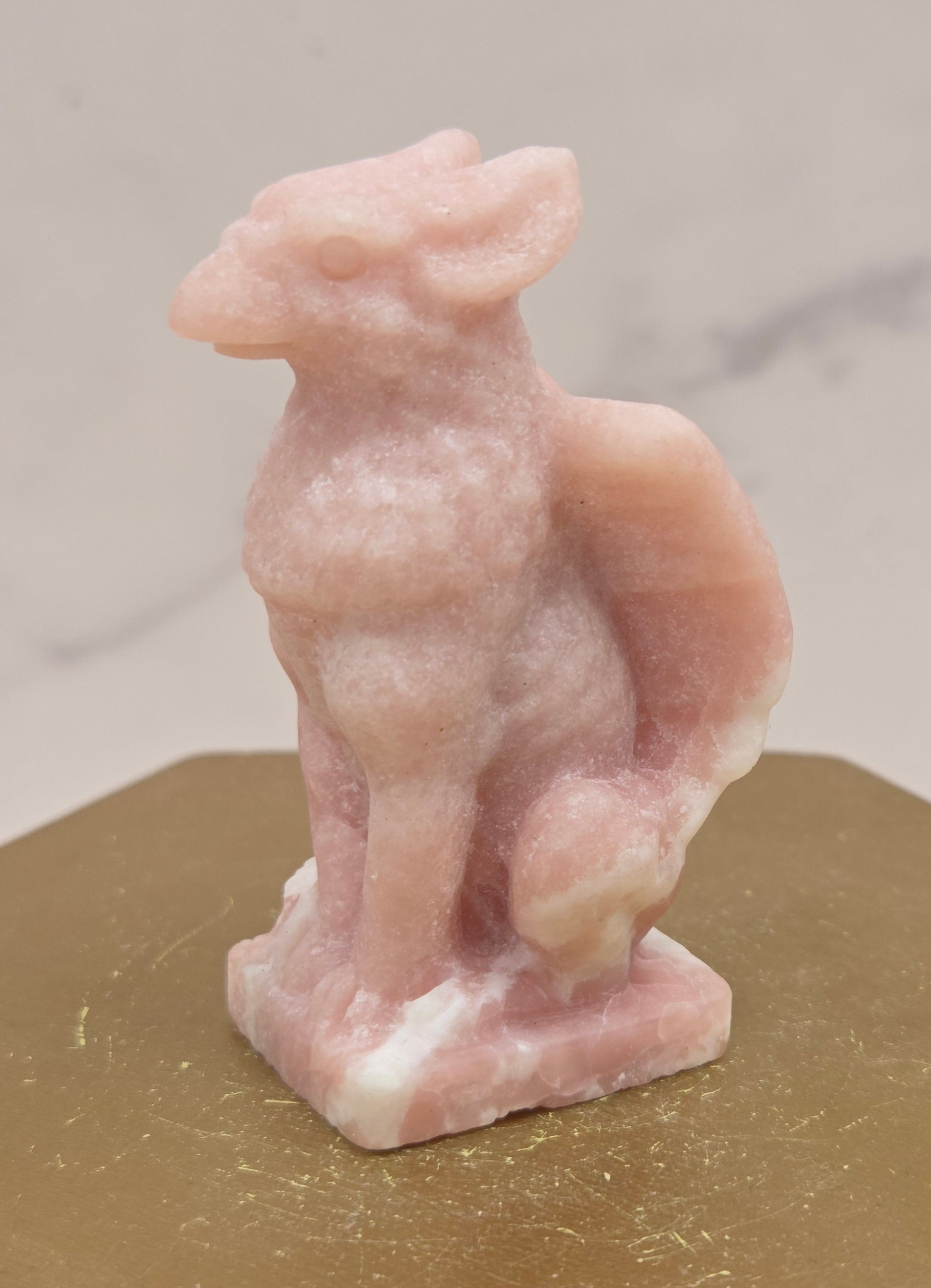 Decorative Pink Opal griffon carving on a wooden surface with a white background
