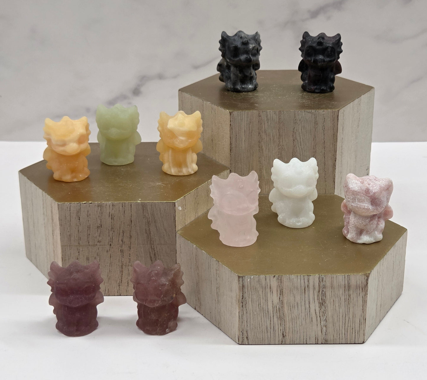 Crystal dragon carvings in a variety of materials and colors on a wooden stand against a white background