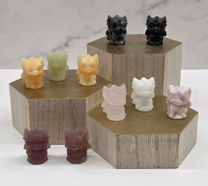 Crystal dragon carvings in a variety of materials and colors on a wooden stand against a white background