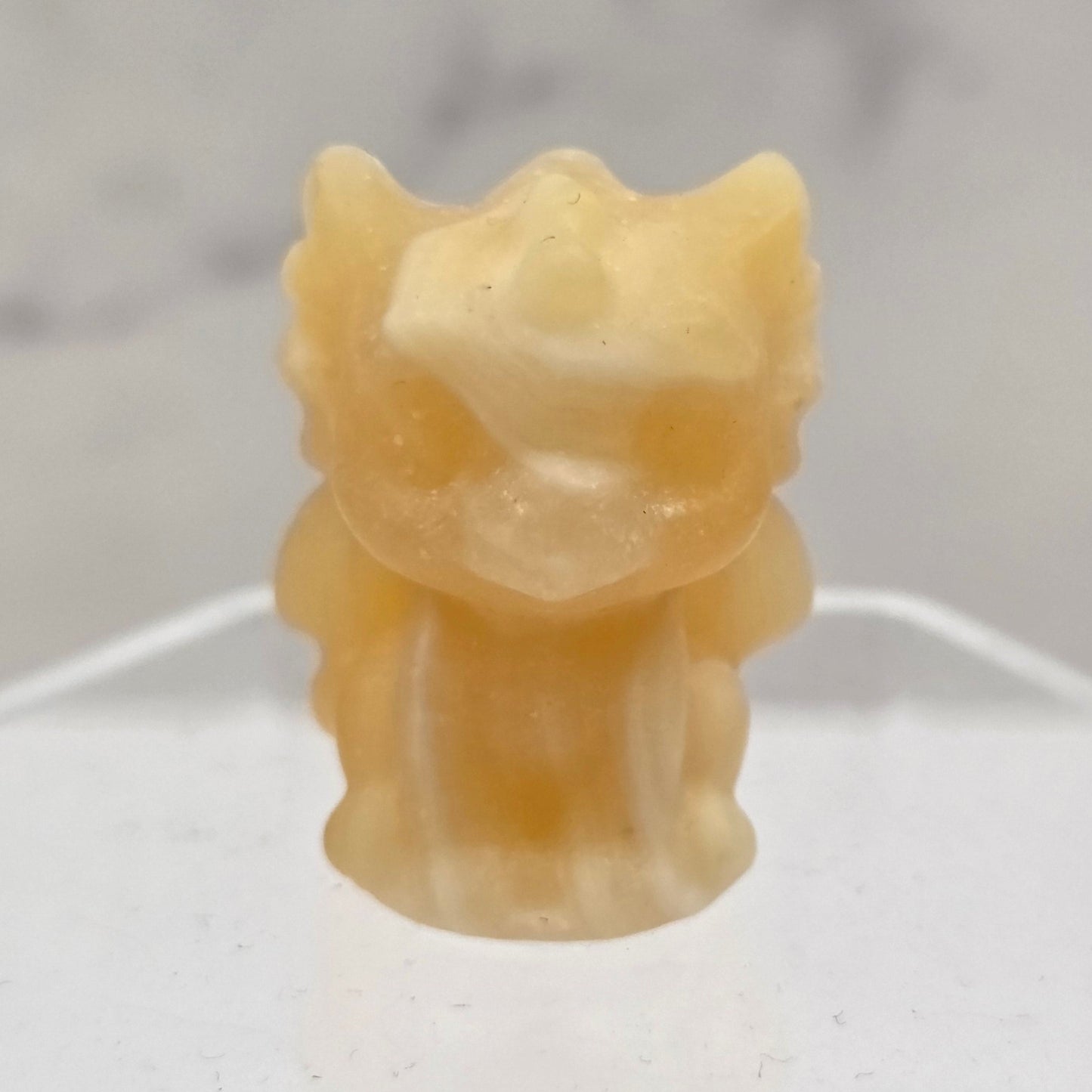 Orange Calcite dragon carving on an acrylic stand against a white background