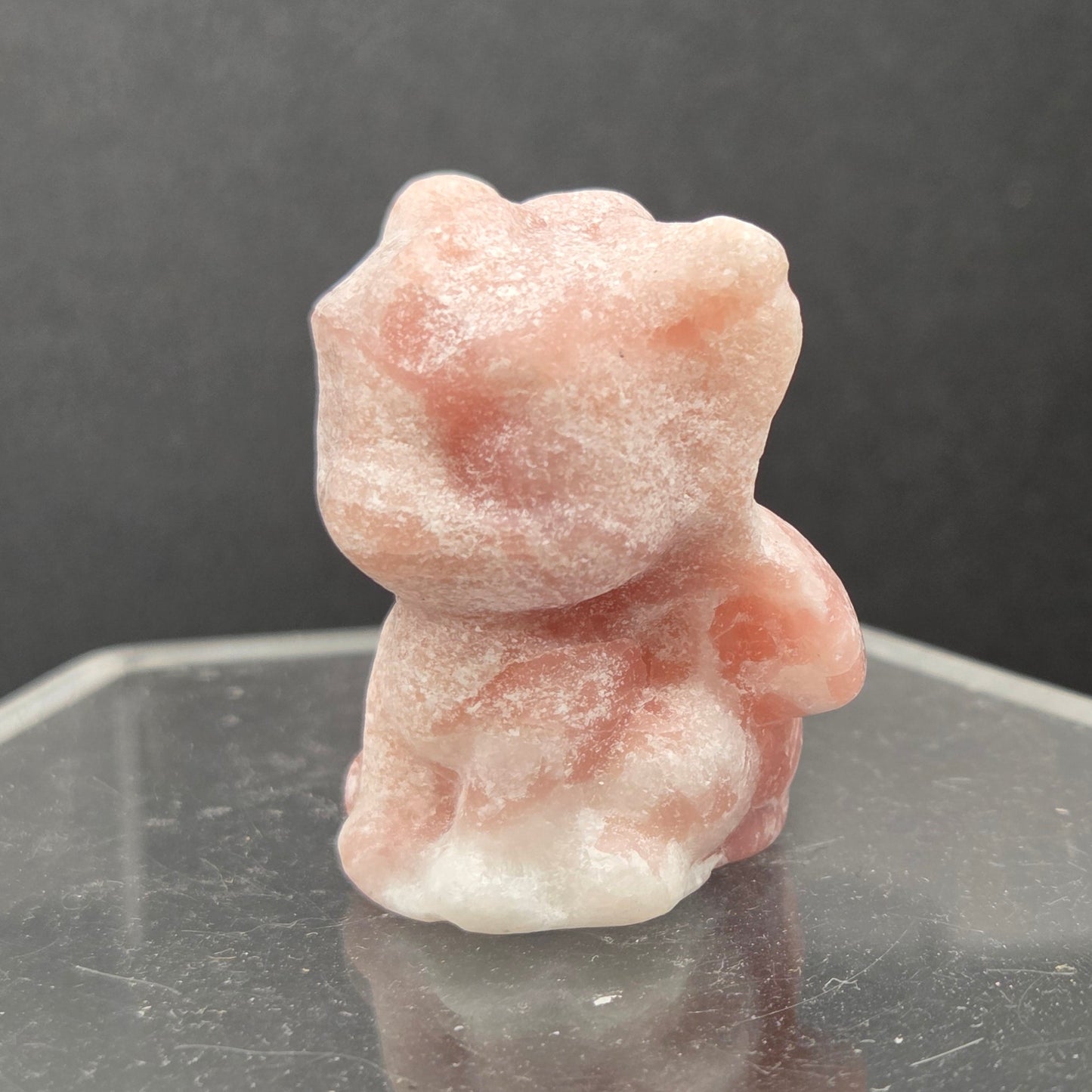 Pink Opal dragon carving on an acrylic stand against a dark background