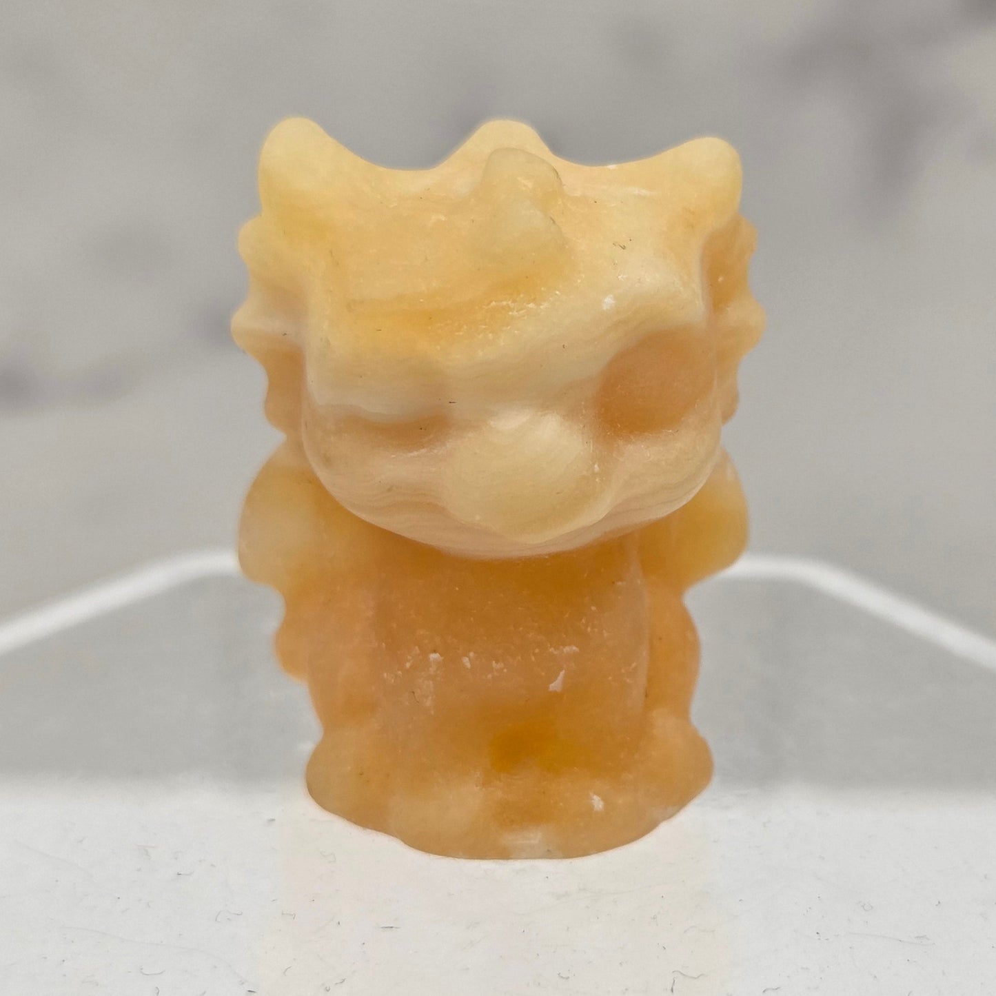 Orange Calcite dragon carving on an acrylic stand against a white background