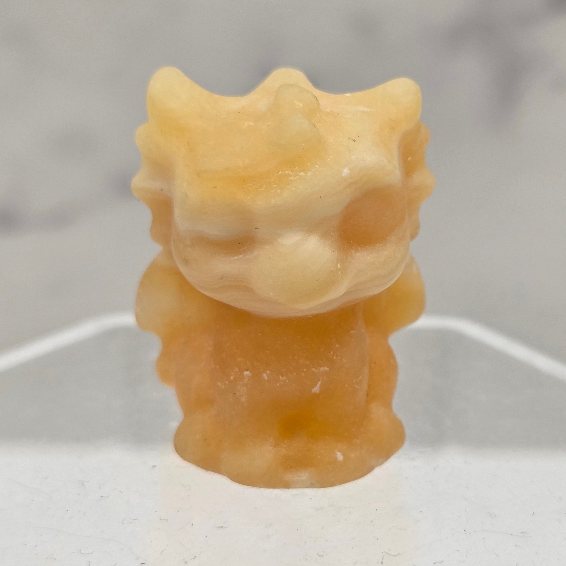 Orange Calcite dragon carving on an acrylic stand against a white background