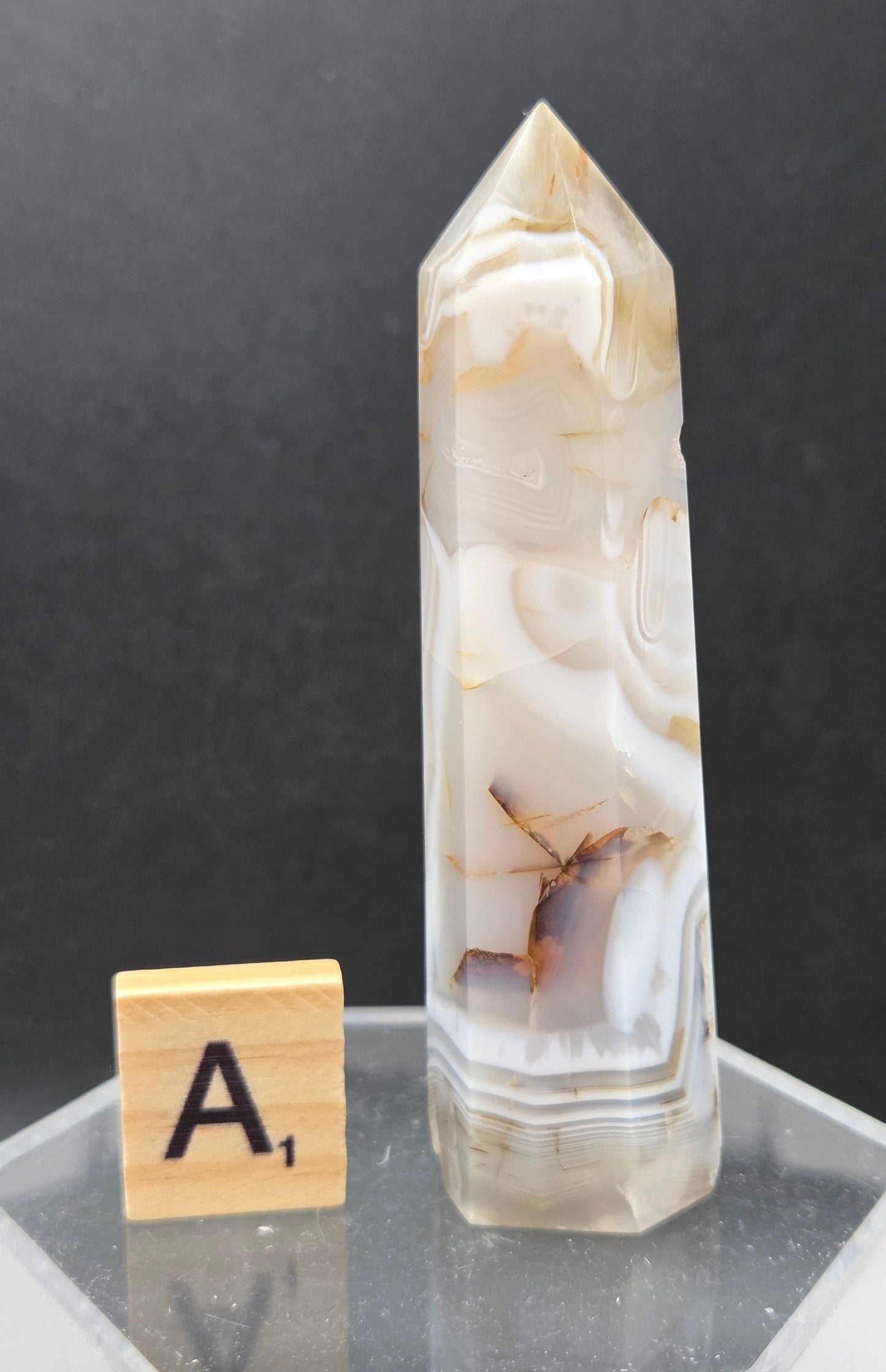 Dendritic Agate tower on an acrylic stand against a dark background