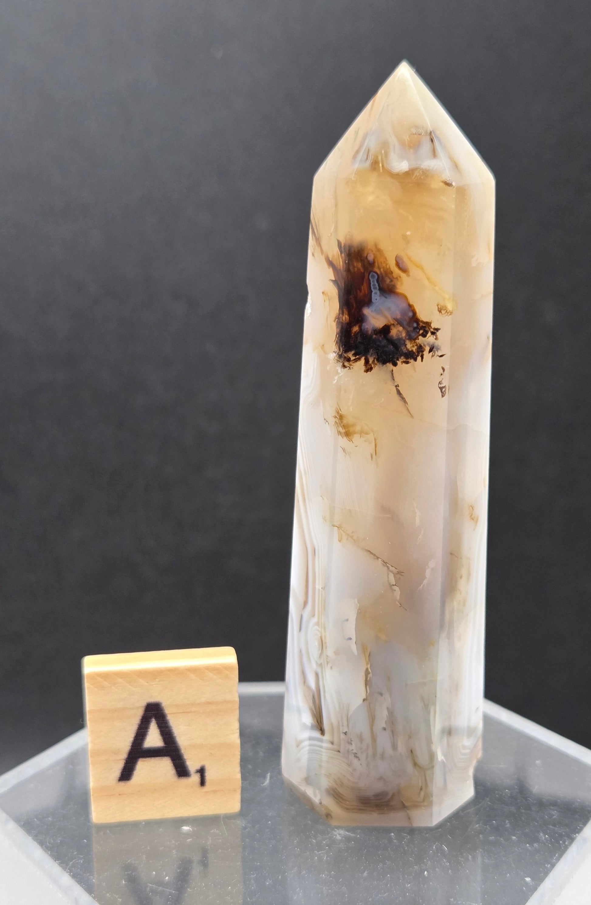 Dendritic Agate tower on an acrylic stand against a dark background