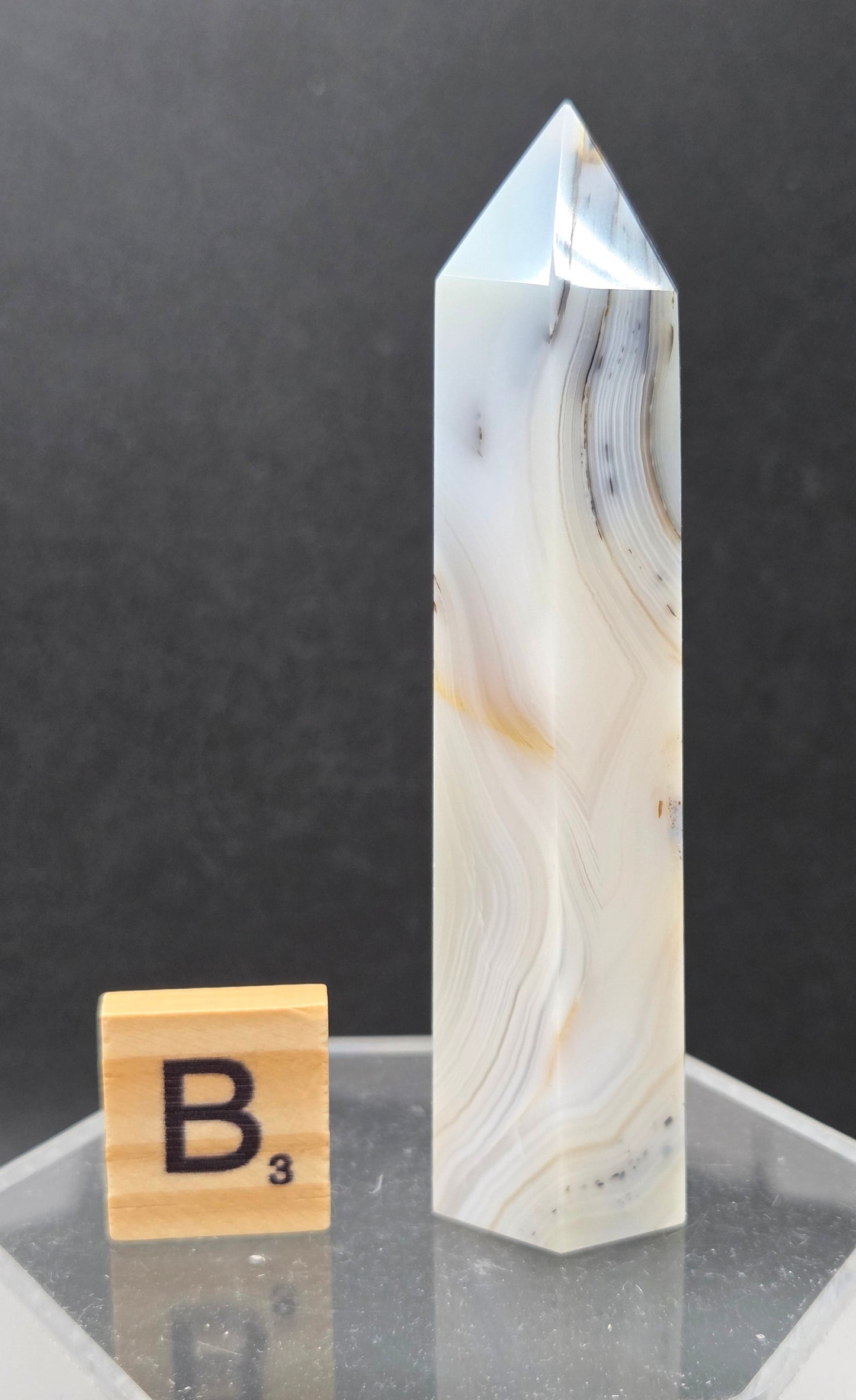 Dendritic Agate tower on an acrylic stand against a dark background