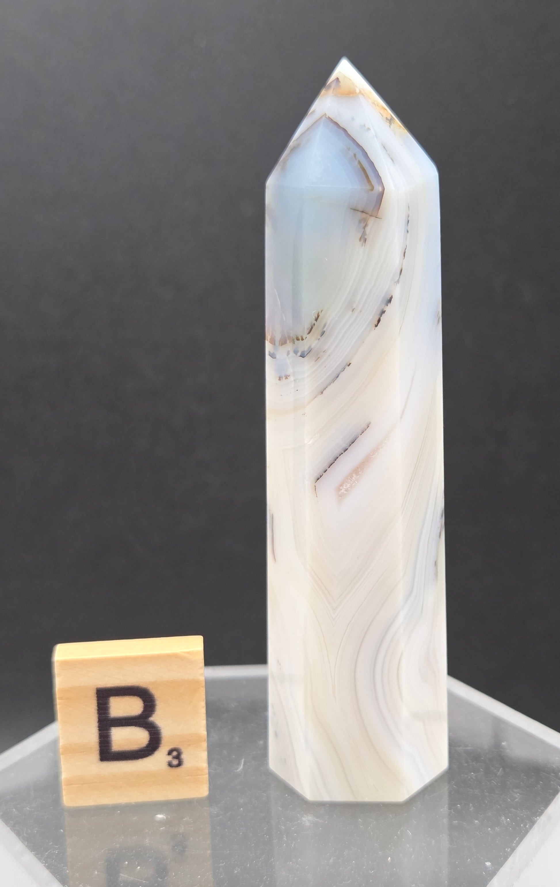 Dendritic Agate tower on an acrylic stand against a dark background