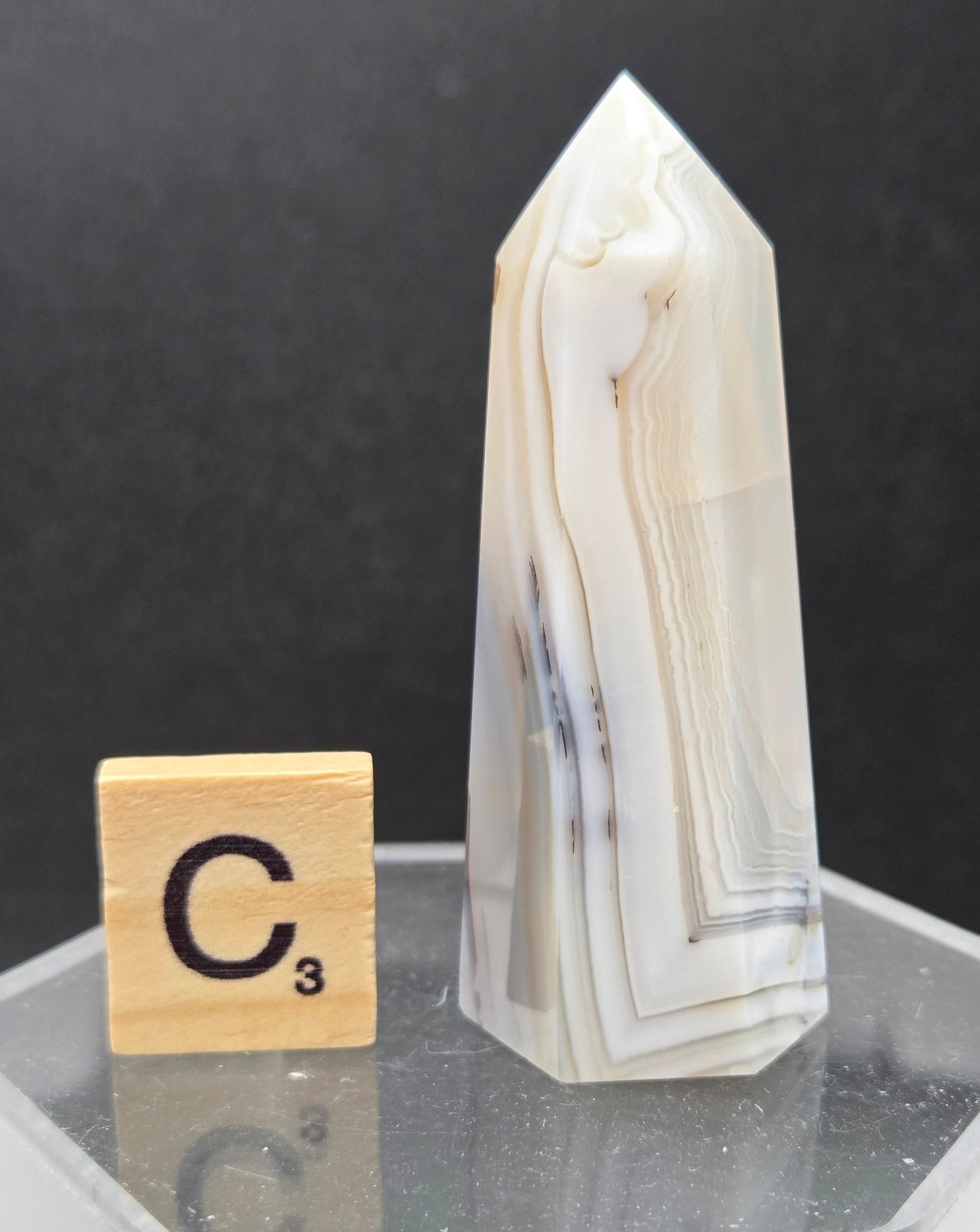 Dendritic Agate tower on an acrylic stand against a dark background
