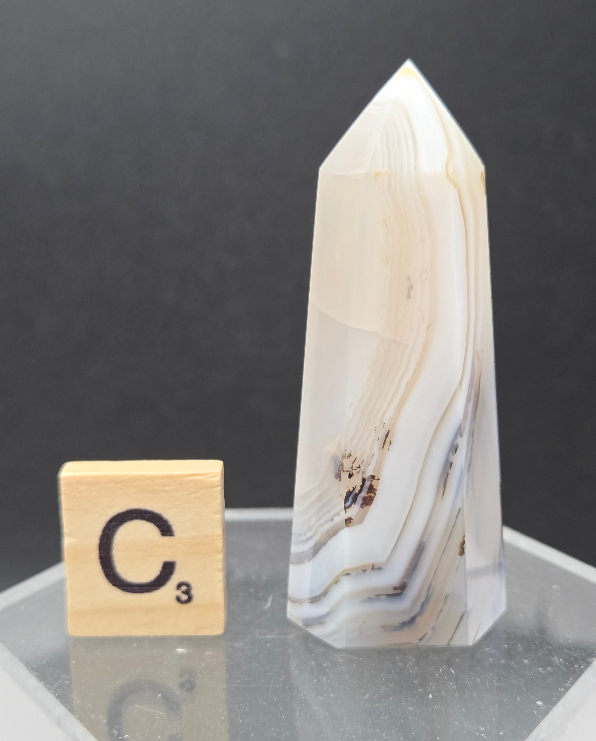 Dendritic Agate tower on an acrylic stand against a dark background