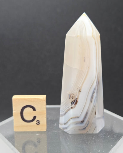 Dendritic Agate tower on an acrylic stand against a dark background