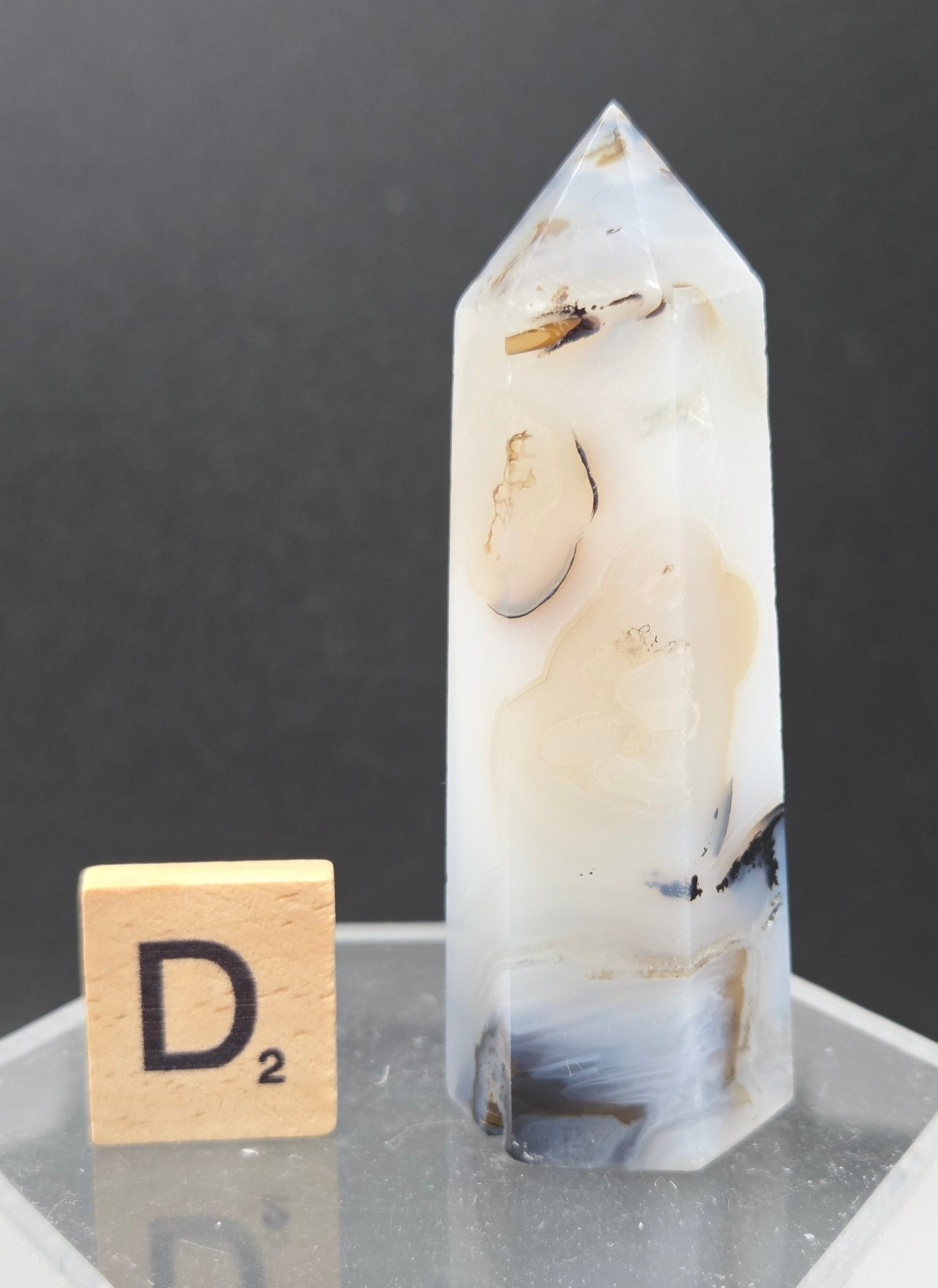 Dendritic Agate tower on an acrylic stand against a dark background