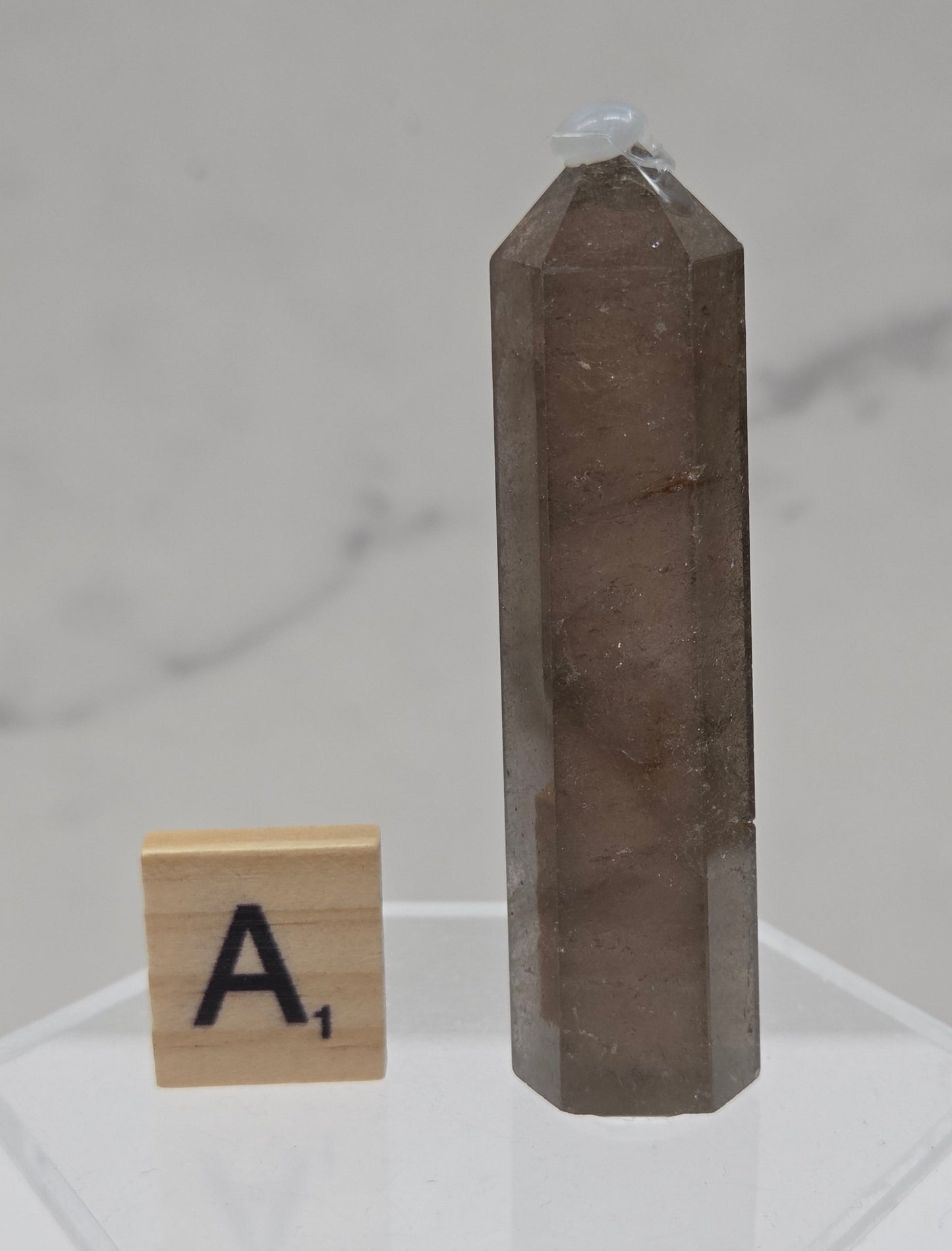 Smoky Quartz crystal on a clear stand with a letter 'A' block against a light background