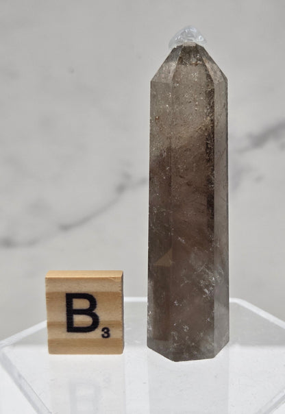 Smoky Quartz crystal on a clear stand with a letter 'B' block against a light background