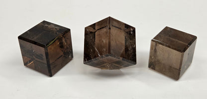 Three smoky quartz cube carvings on a white background