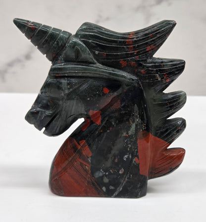 Decorative unicorn carving made of African Bloodstone with black and red design on a white marble background