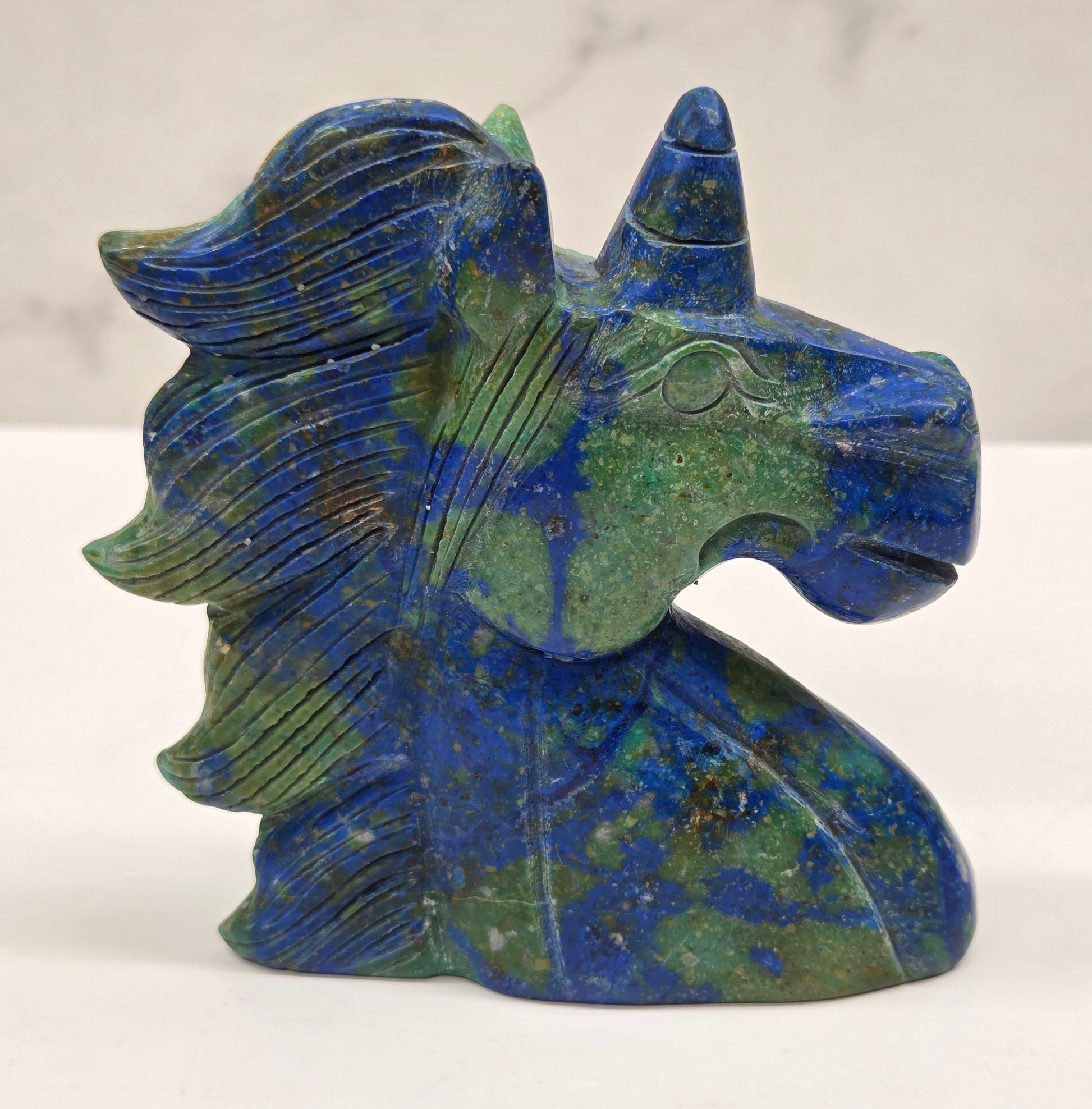 Carved stone unicorn figurine with blue and green patterns on a white background