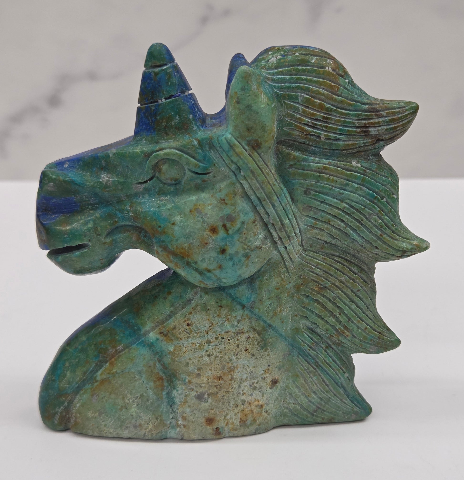 Carved stone unicorn figurine with blue and green patterns on a white background