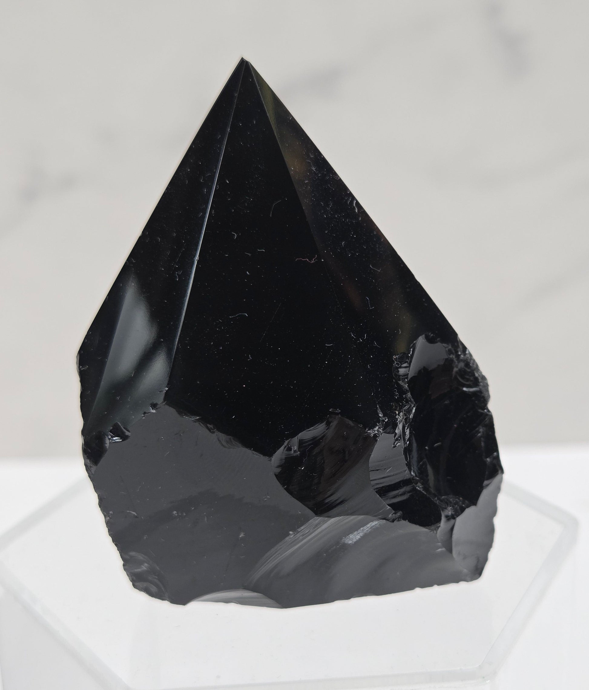 black Obsidian half polished point on a white surface with a gray marble background