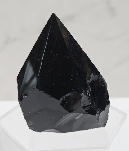 black Obsidian half polished point on a white surface with a gray marble background