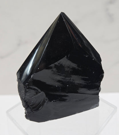 black Obsidian half polished point on a white surface with a gray marble background