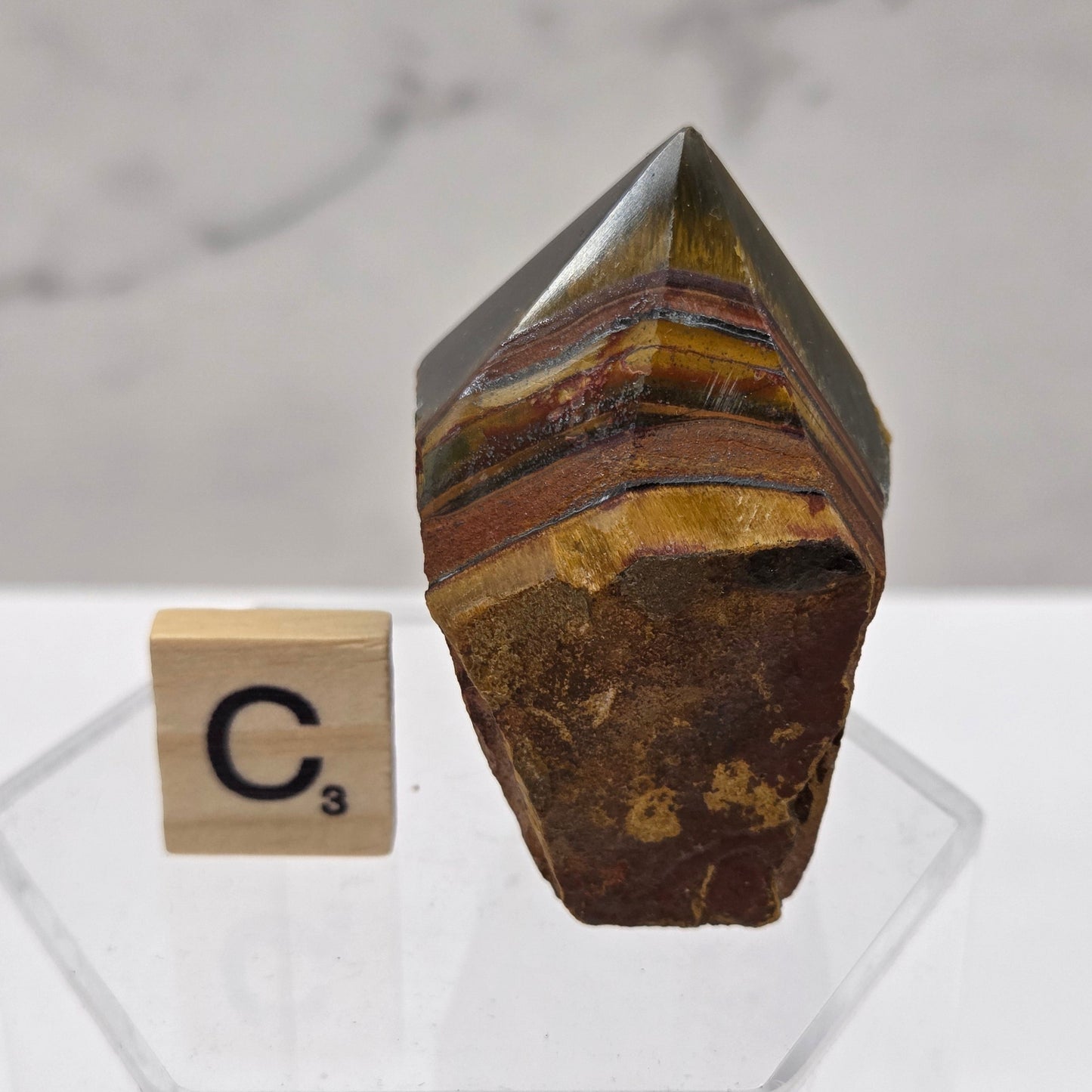 Tigers Eye specimen on a white background with a small wooden block displaying 'C' 