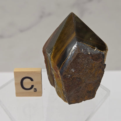 Tigers Eye specimen on a white background with a small wooden block displaying 'C' 