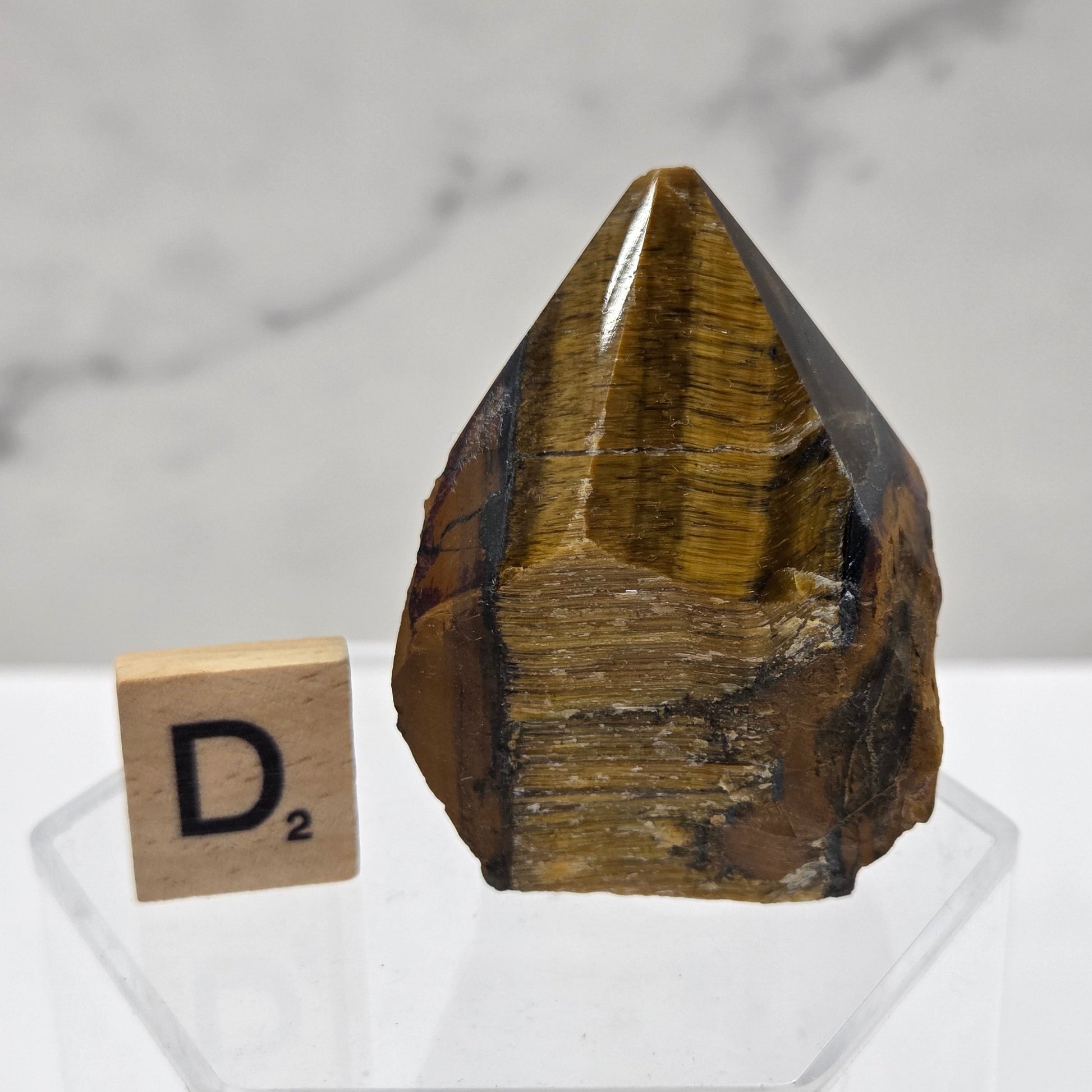 Tigers Eye specimen on a white background with a small wooden block displaying 'D' 