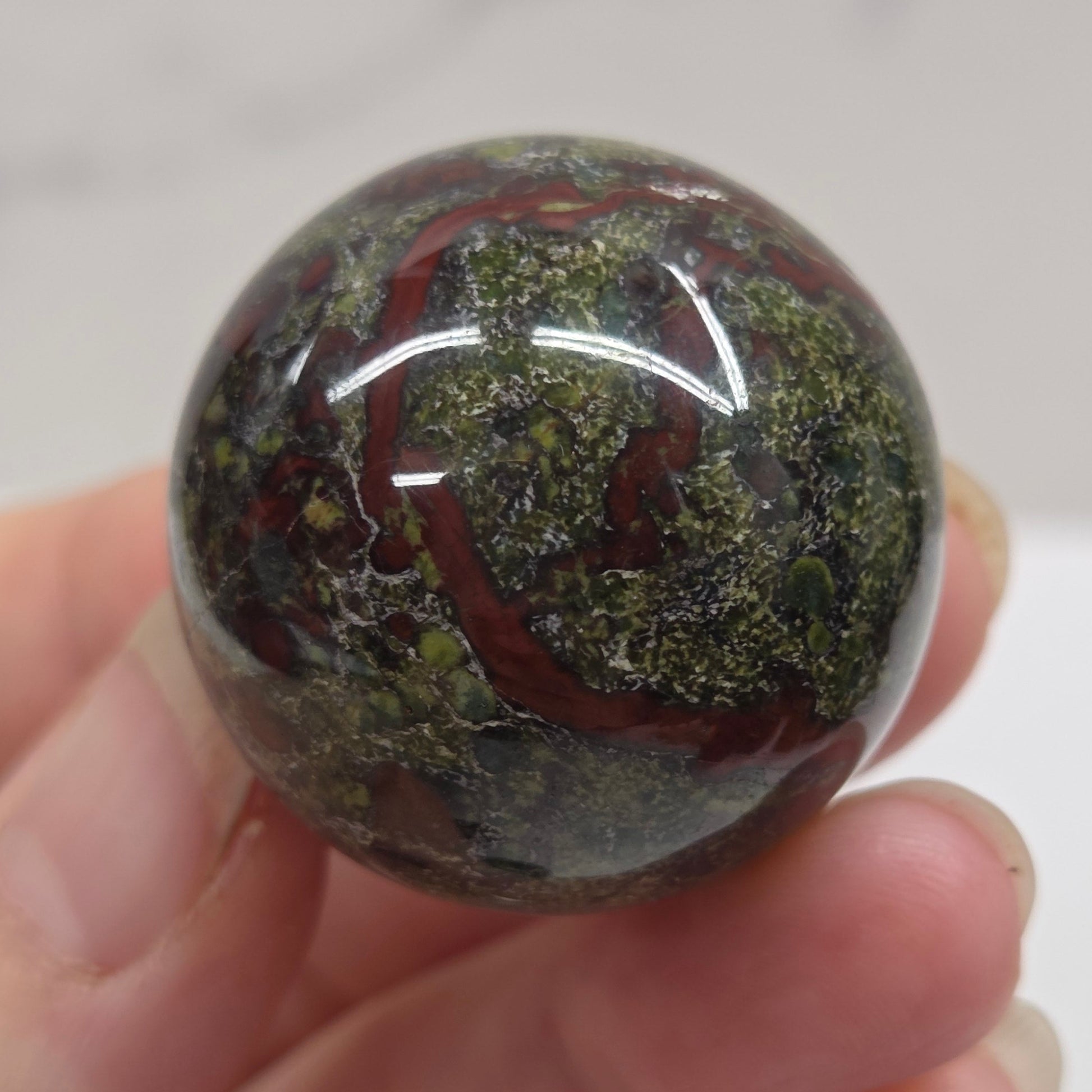 Hand holding a dragons blood sphere  with green and red patterns against a plain background