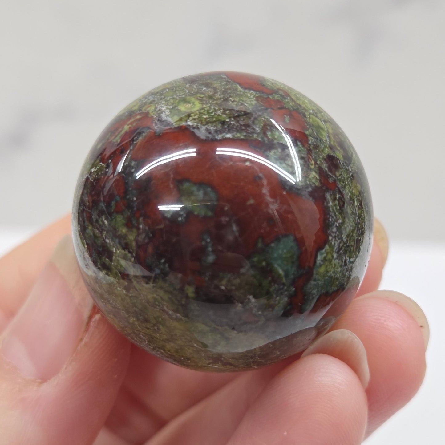 Hand holding a dragons blood sphere  with green and red patterns against a plain background