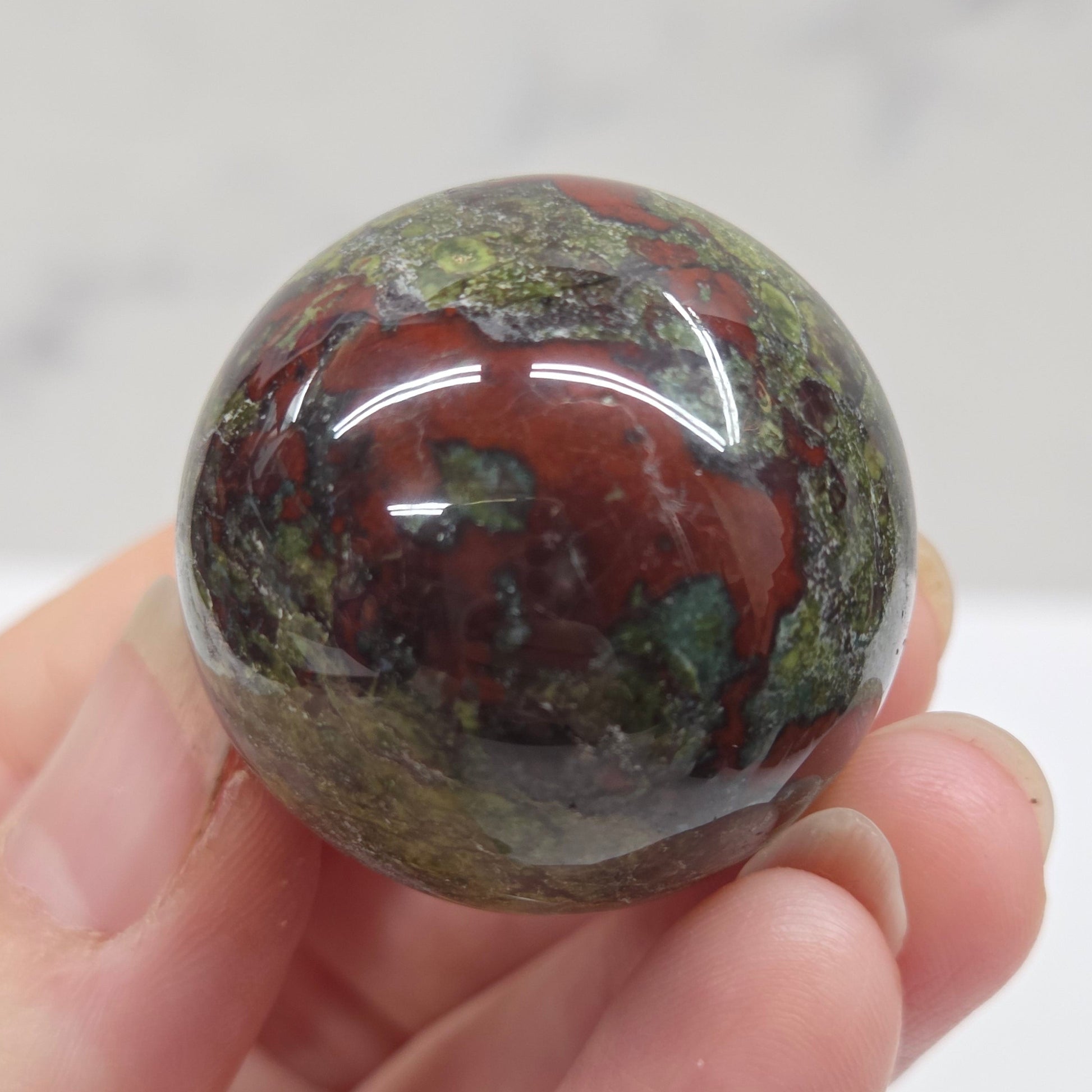 Hand holding a dragons blood sphere  with green and red patterns against a plain background