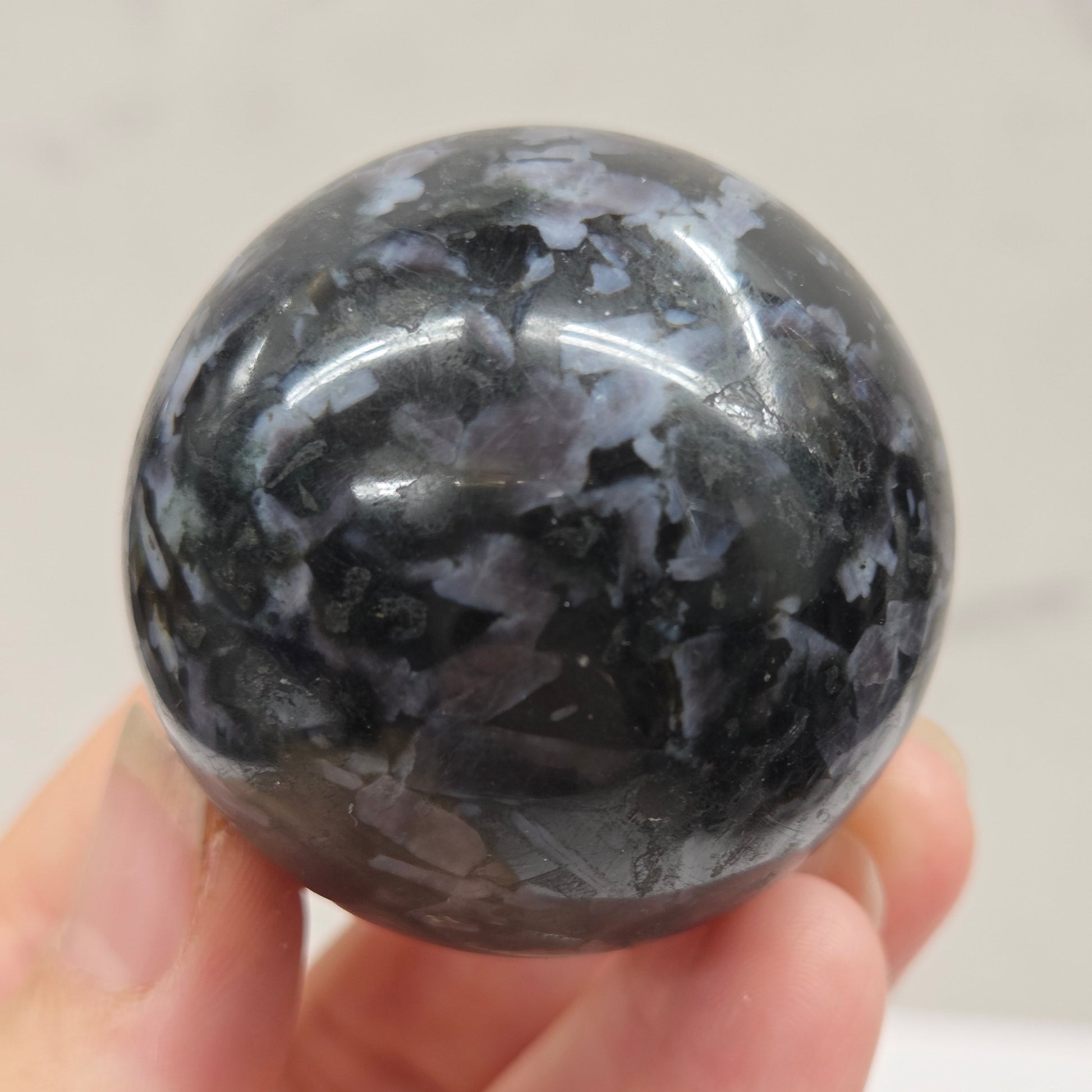 Person holding a dark marbled crystal sphere against a neutral background