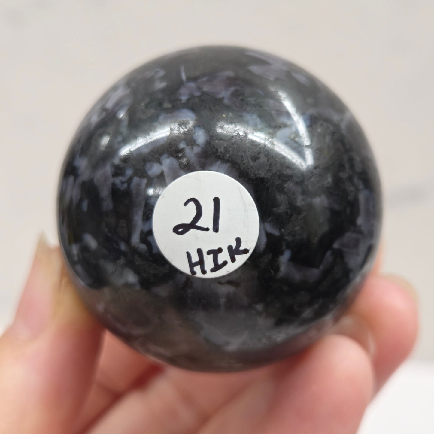 Person holding a dark marbled crystal sphere against a neutral background