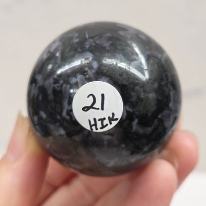 Person holding a dark marbled crystal sphere against a neutral background
