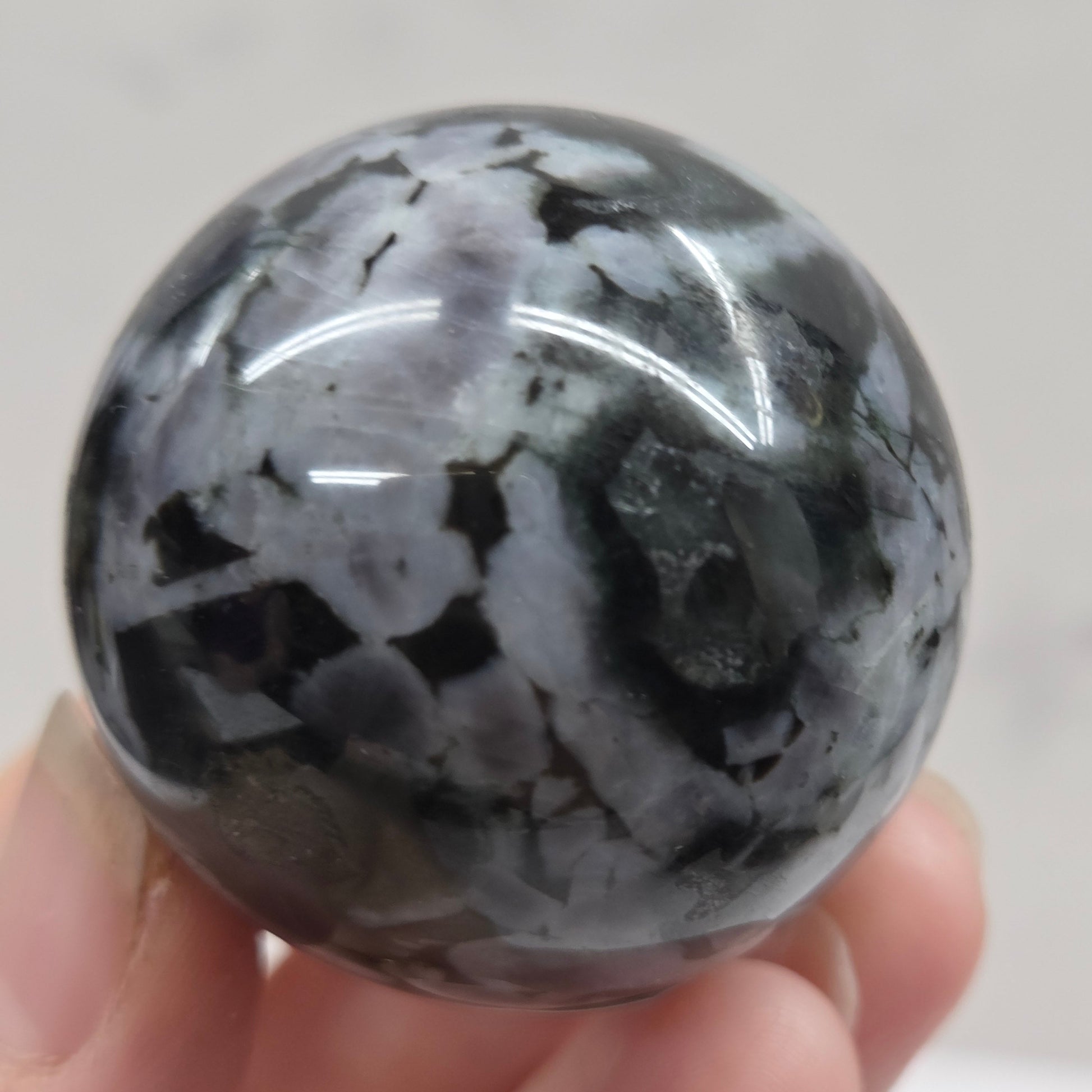 Person holding a dark marbled crystal sphere against a neutral background