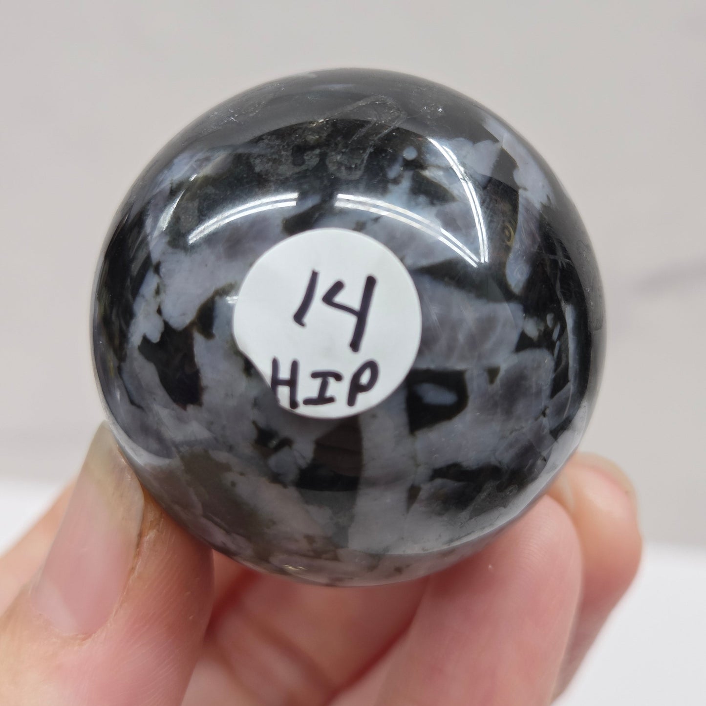 Person holding a dark marbled crystal sphere against a neutral background
